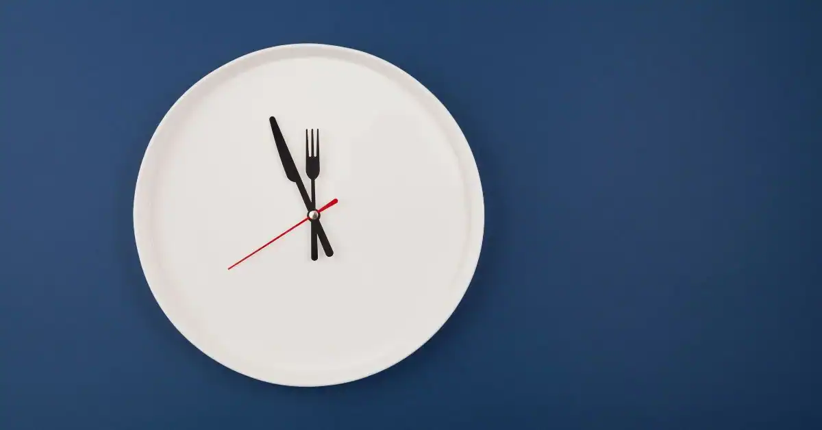 A white plate serving as a clock face with a knife and fork as hands, set against a blue background, indicating the time.