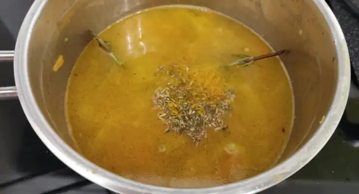 A metal pot on a stove with a yellow broth of cooking red lentils, topped with fresh herbs and spices